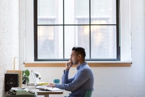 man sitting at his desk in front of his window thinking while loooking ata his computer